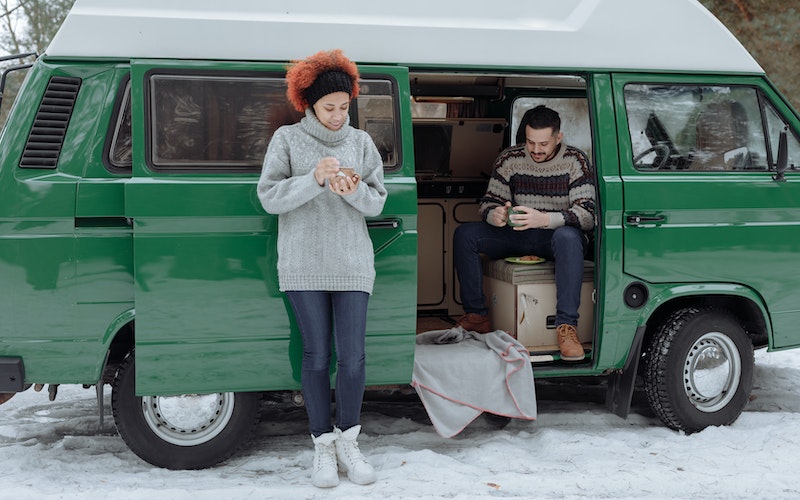 two people standing in the snow in front of a green van